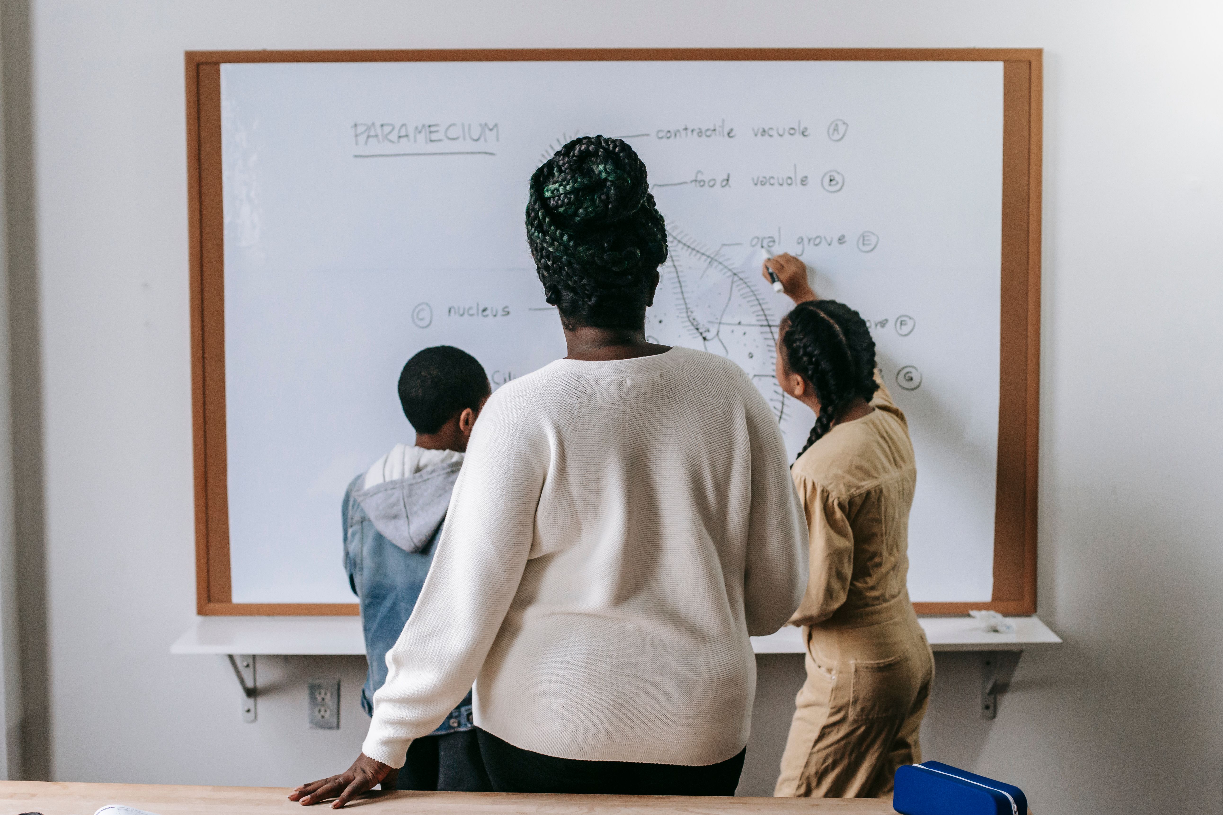 Female teacher helping students write on classroom whiteboard
